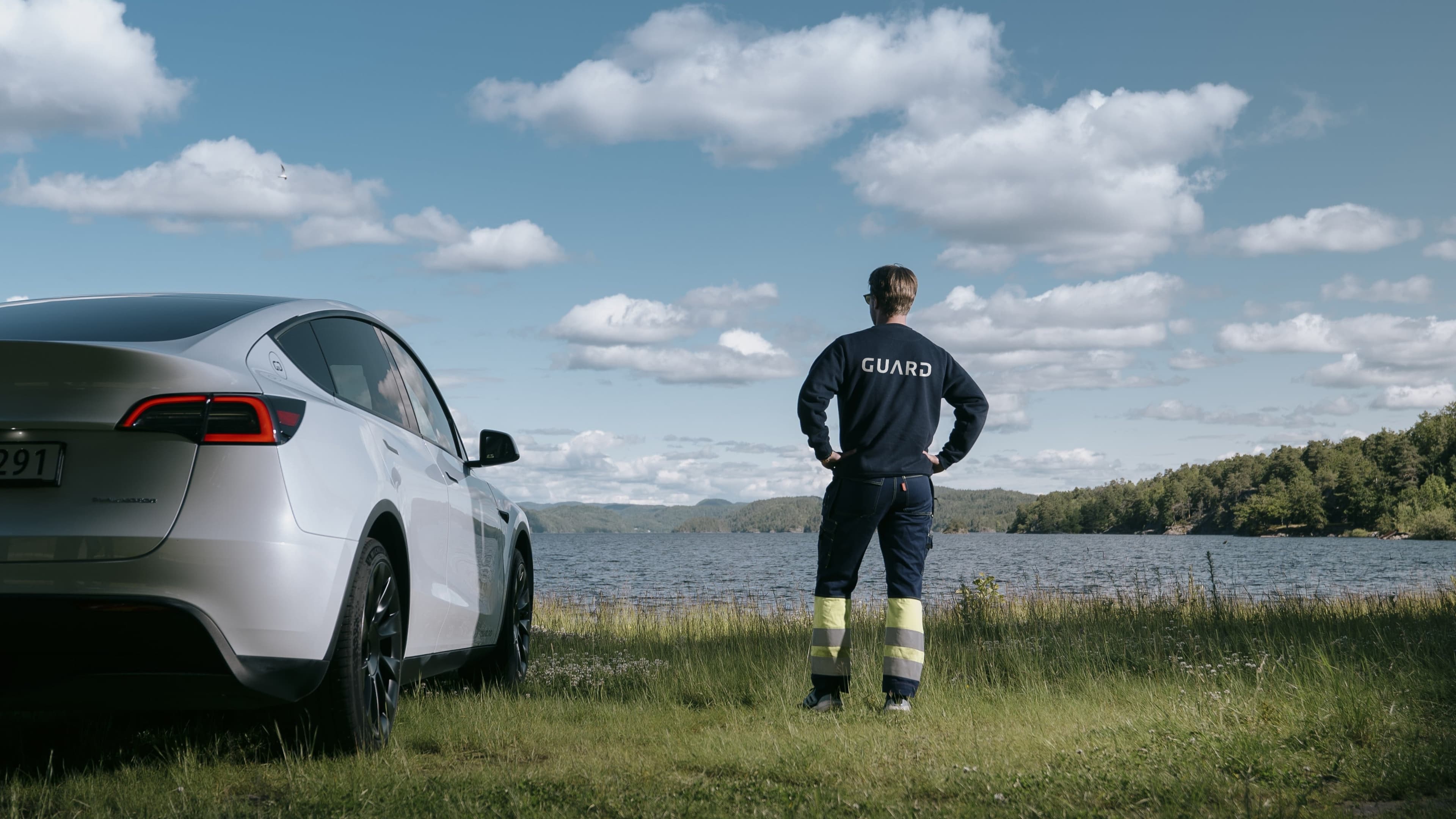Guard employee looking out over the water, a company car beside him